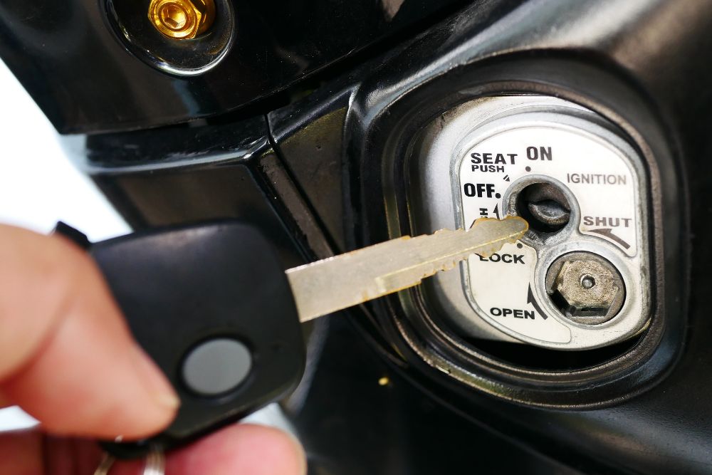 Motorcycle key being inserted into the ignition. Text: SEAT, OFF, LOCK, ON, IGNITION, OPEN, SHUT. Turn Key Locksmith, Phoenix AZ